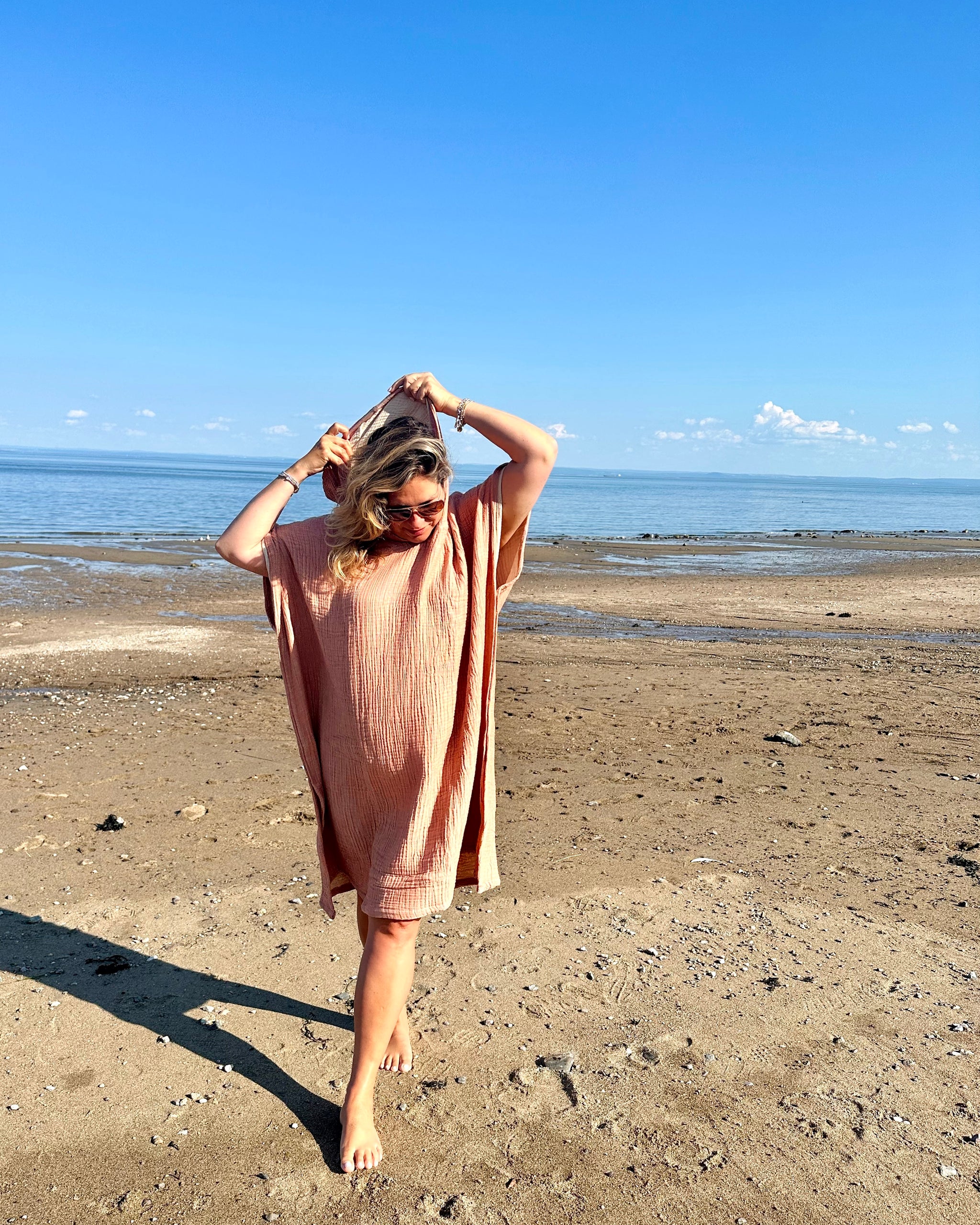 Une femme vêtue du poncho Mia terre cuite marchant sur la plage