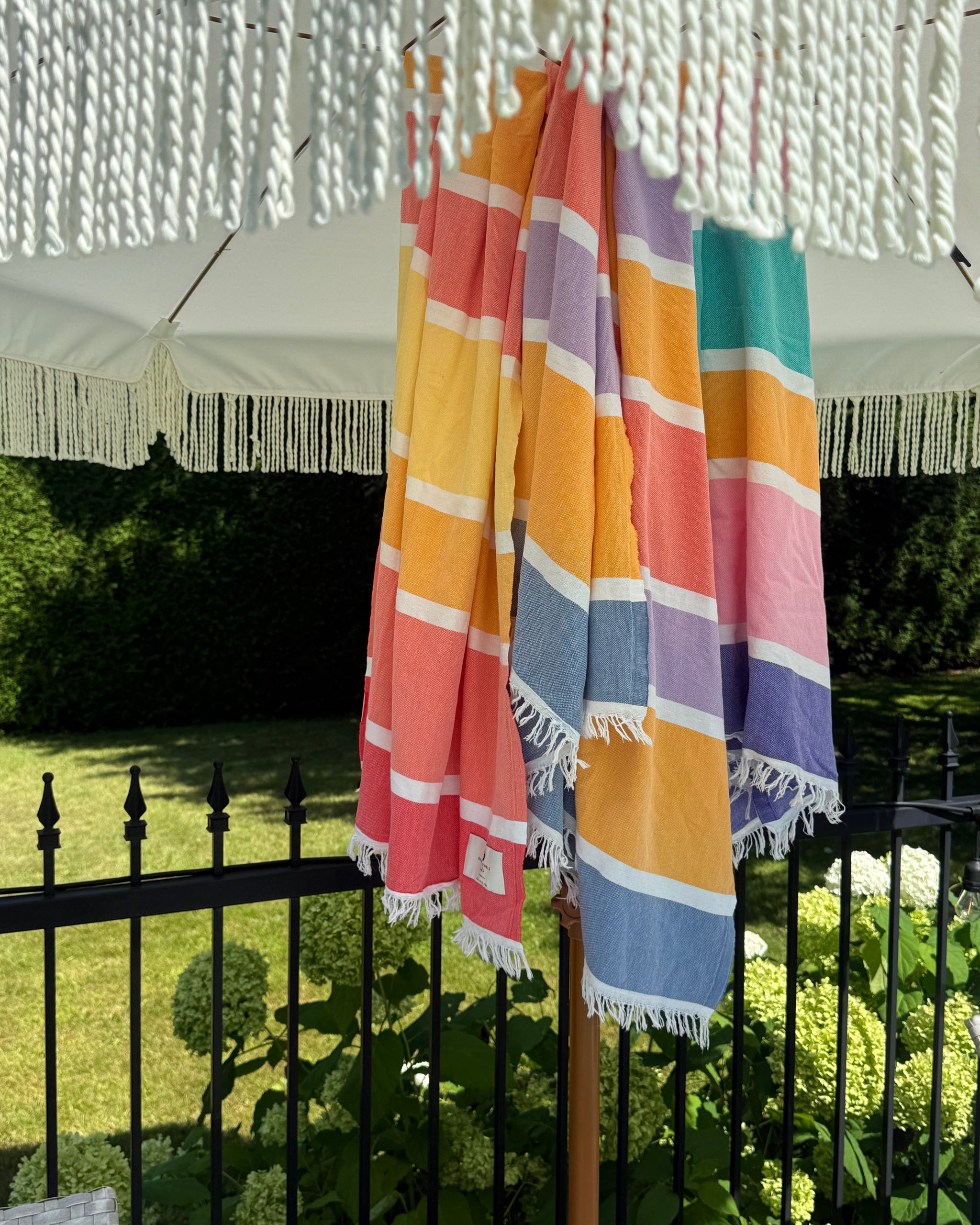 Des serviettes Candy suspendues à une clôture sous un parasol de jardin