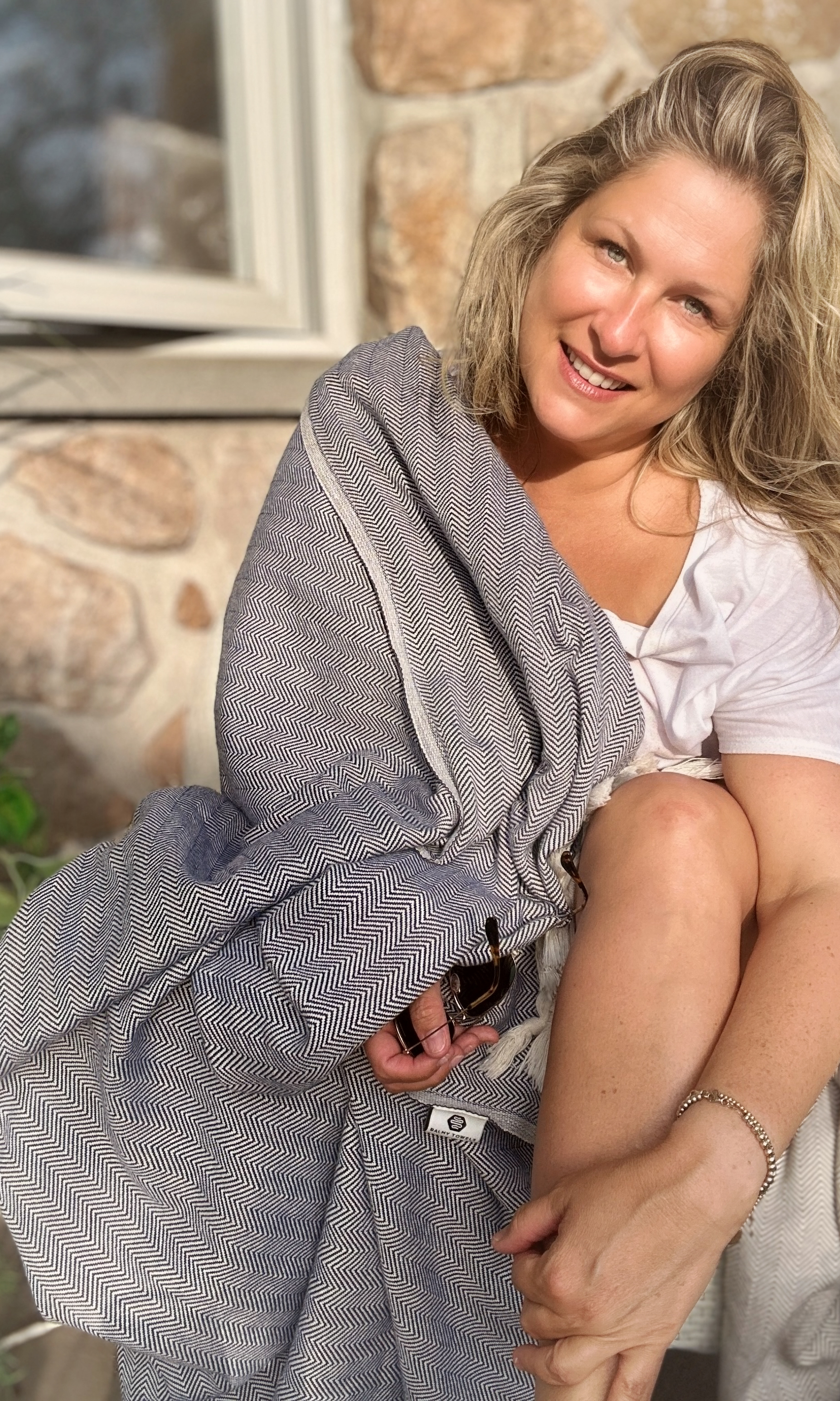 Saskia Thuot enveloppée dans le jeté LIONEL bordeaux, dans un fauteuil en rotin sur sa véranda