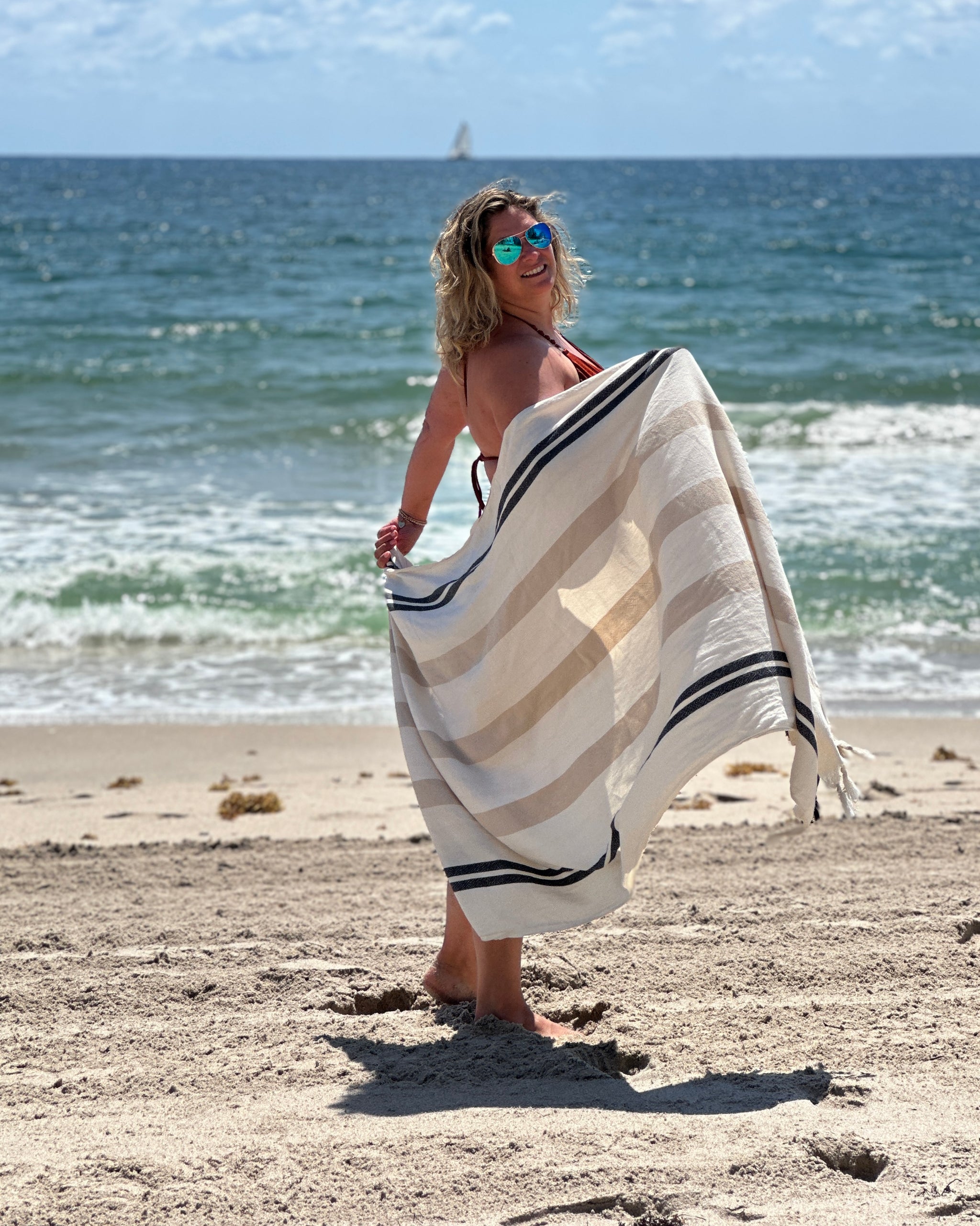 Femme sur une plage tenant ouverte une serviette SIENNA rayée à franges