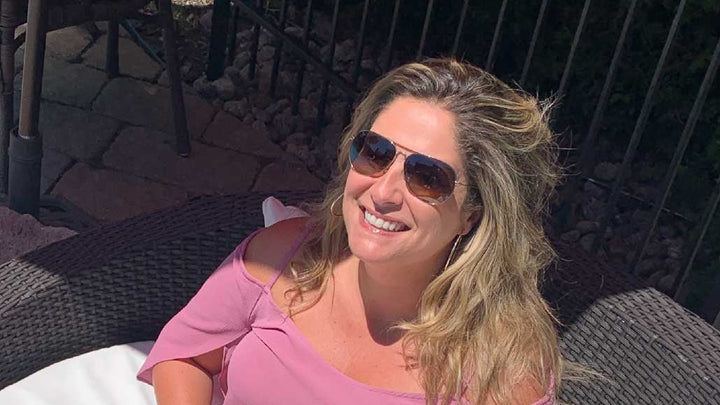 Saskia Thuot, lunettes de soleil aviateur et haut rose, sourit au soleil, assise dans sa cour