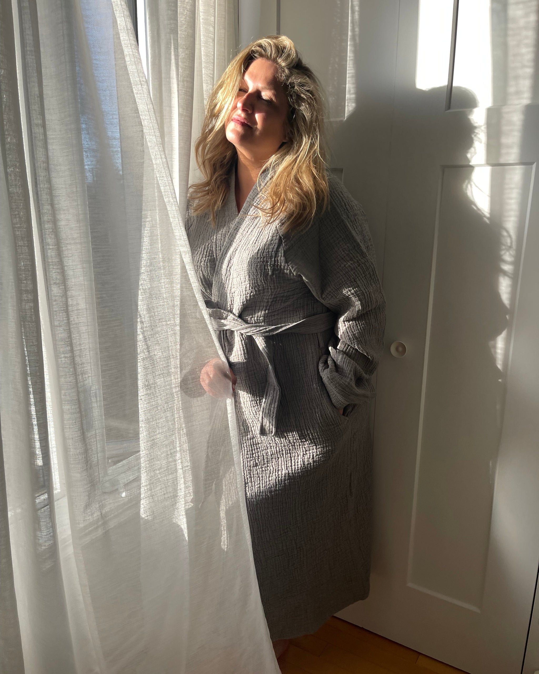 Une femme vêtue du peignoir Bella charbon près d'une fenêtre lumineuse