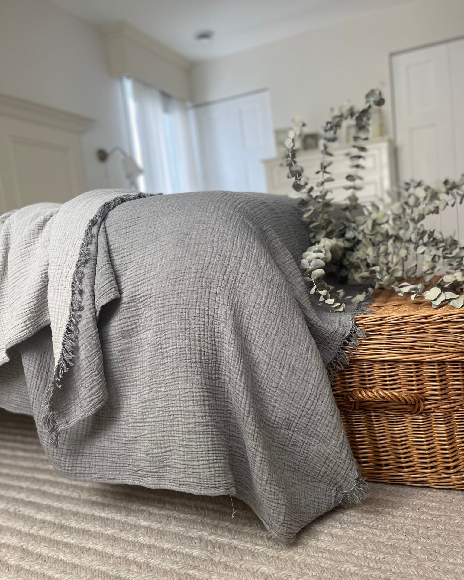 Jeté gris sur le coin d'un lit, panier en osier et branches séchées