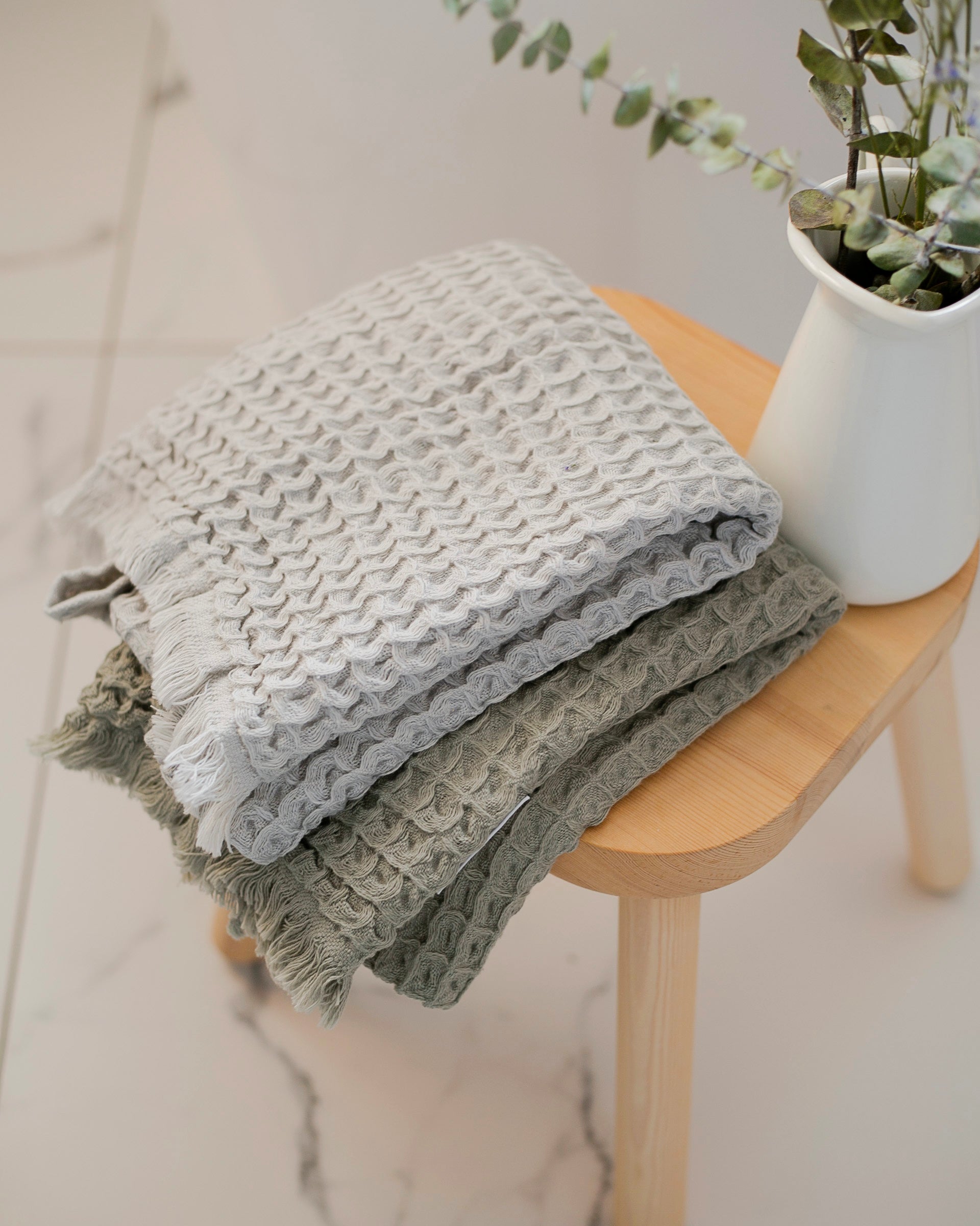 Serviettes à mains pliées sur un tabouret en bois, sous une plante verte