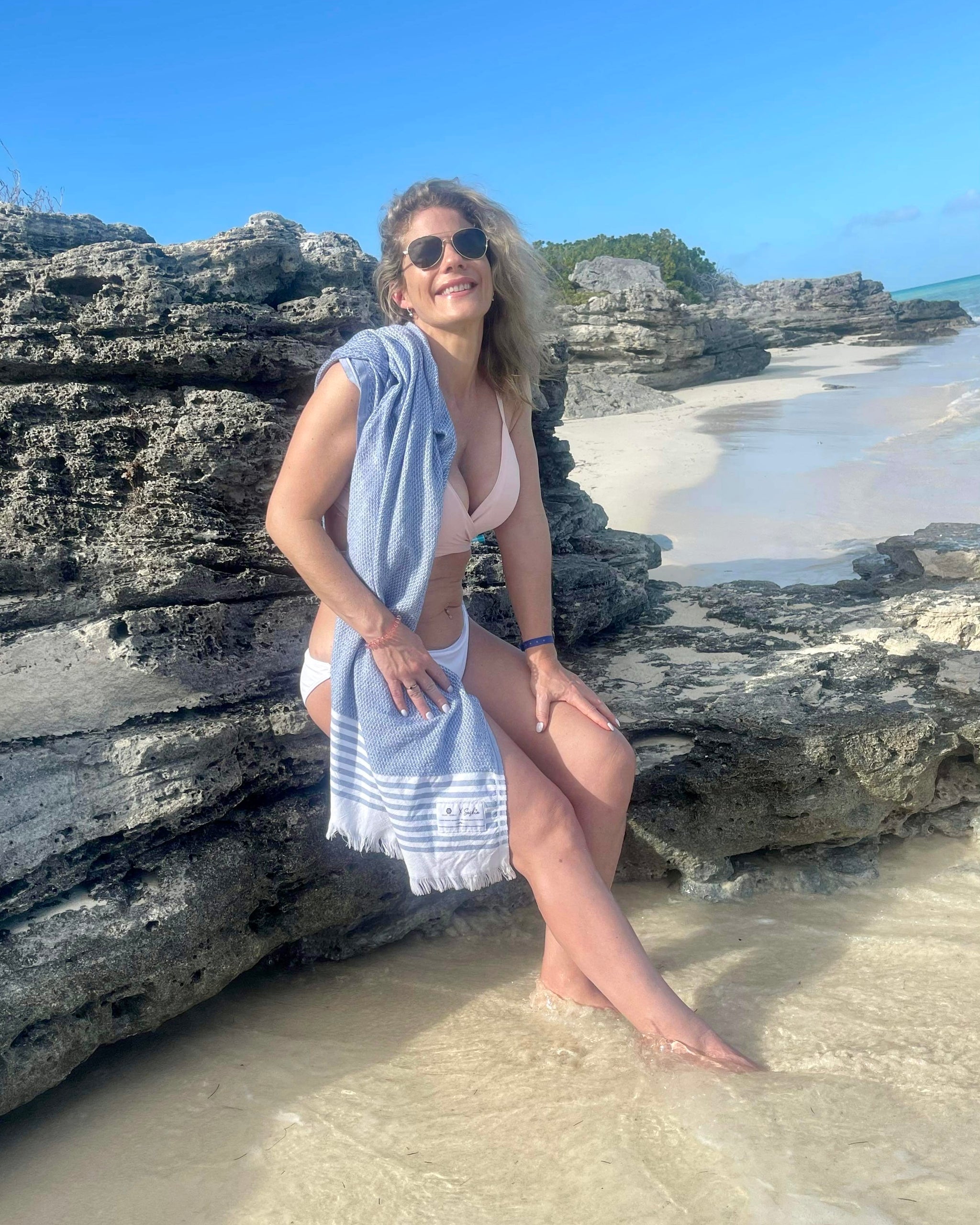 Une femme assise sur des rochers au bord de la mer avec une serviette Gabby