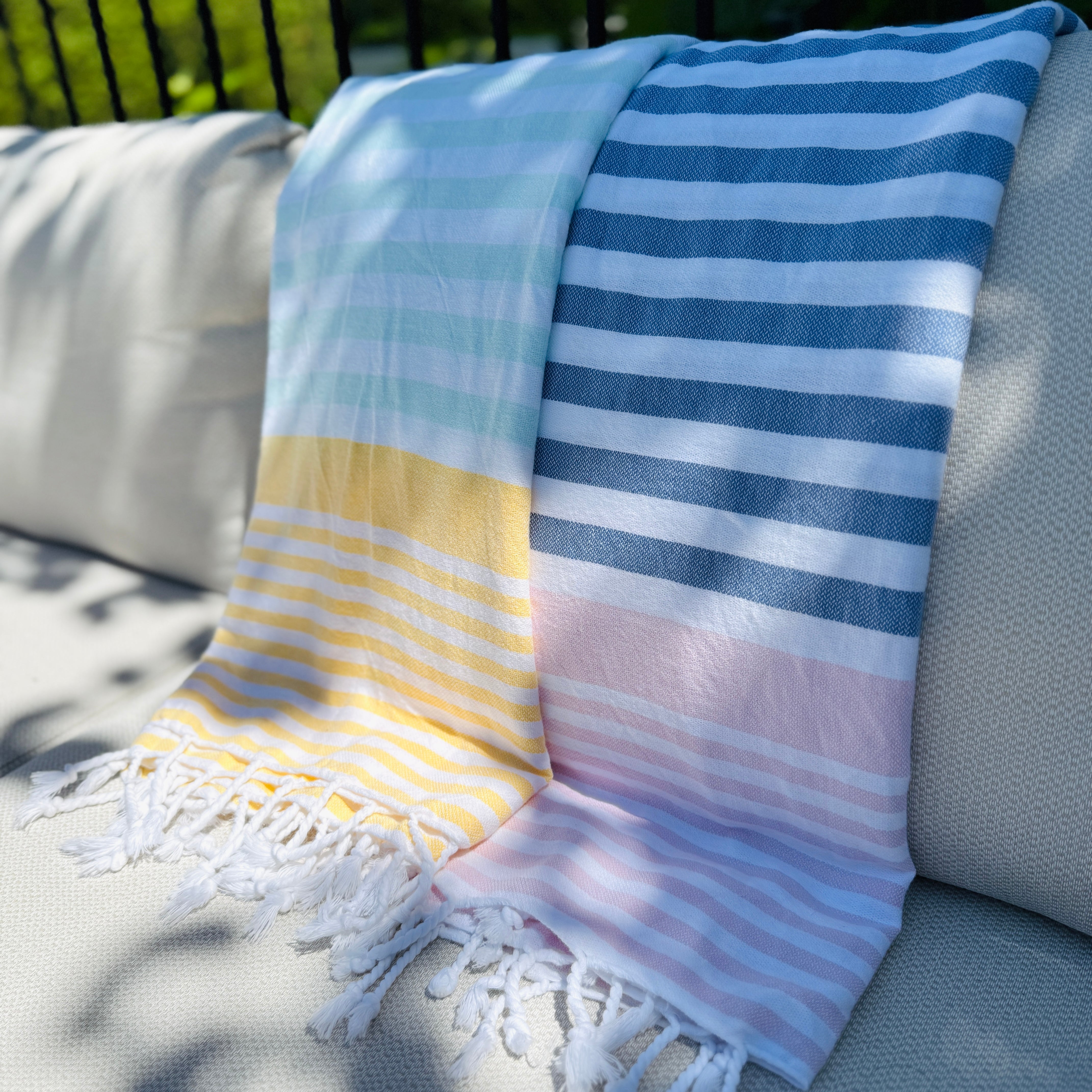 LOLITA towel with colorful pastel stripes and fringes on a sunlit outdoor couch.