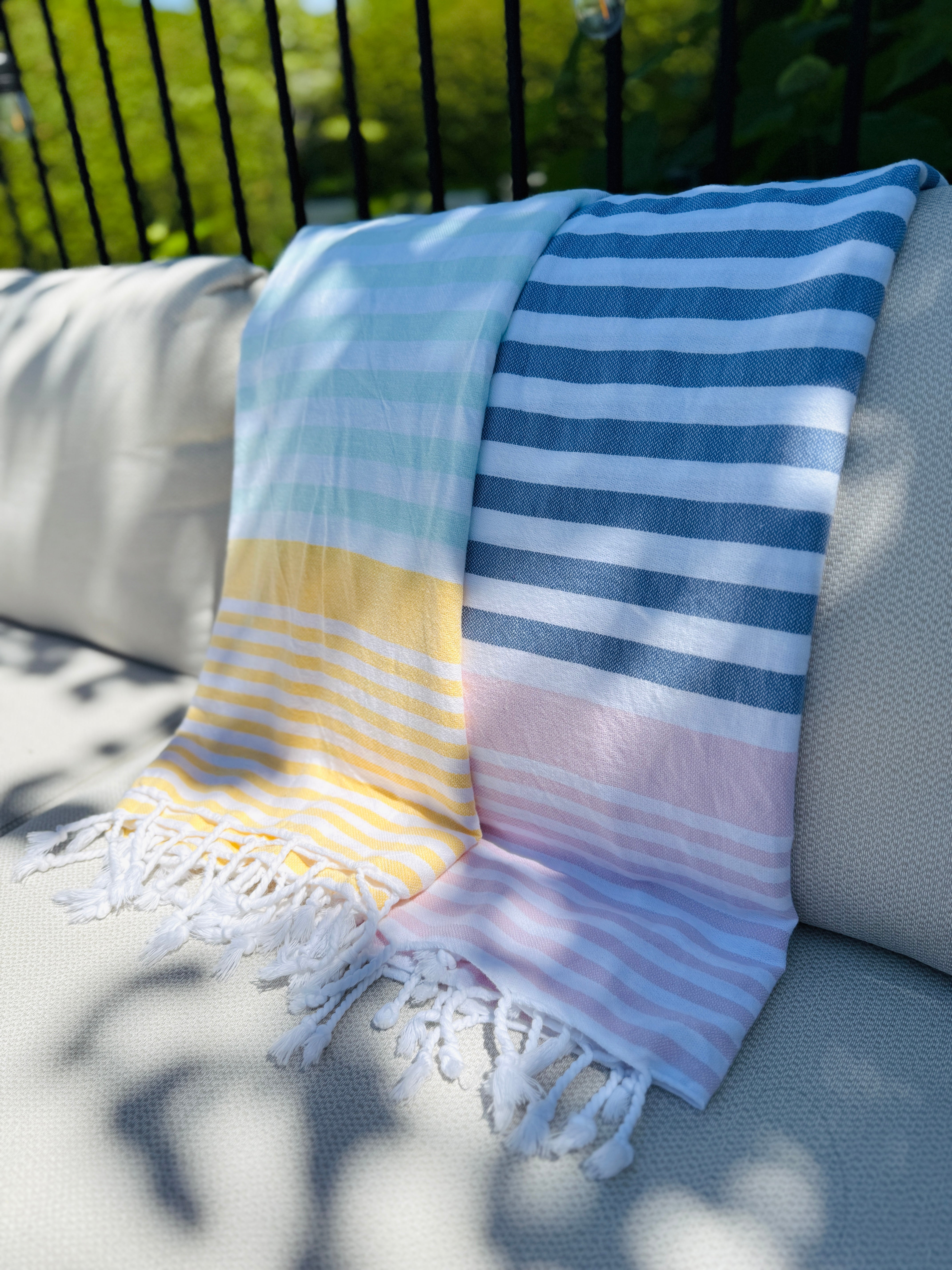 LOLITA towel with colorful pastel stripes and fringes on a sunlit outdoor couch.
