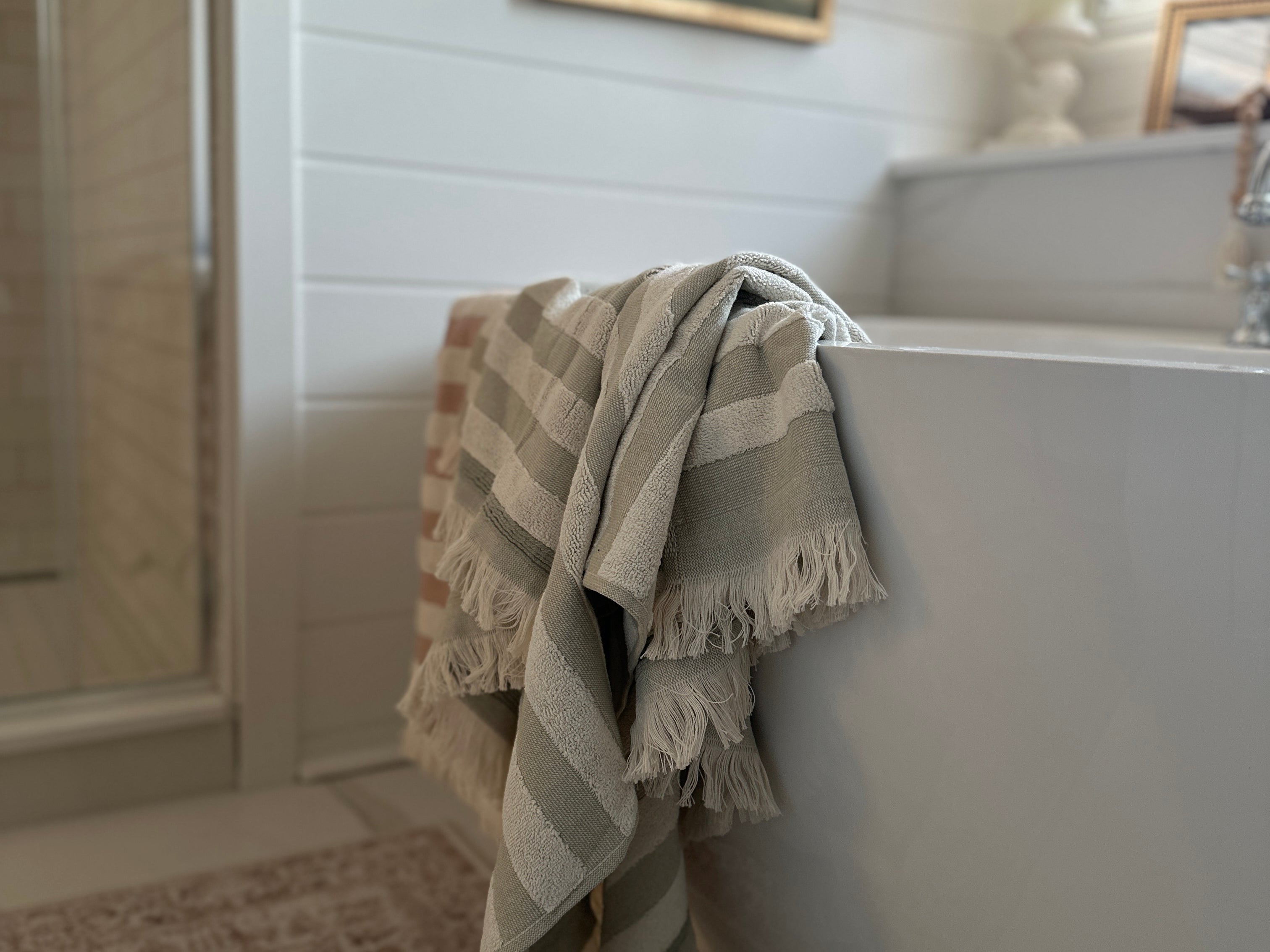 Billie towel in Green Tea  and pink draped over a bathtub in a soft, sunlit bathroom