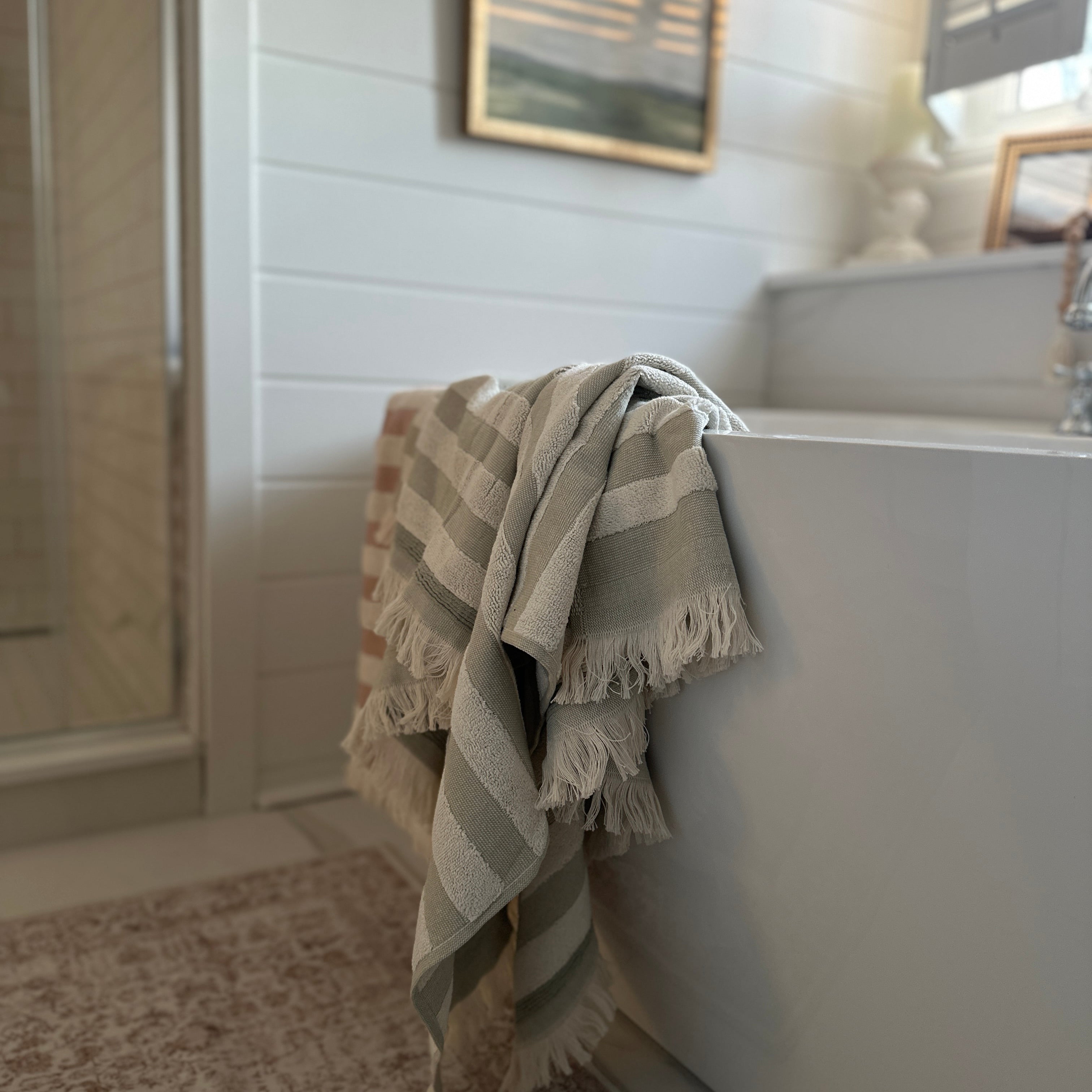 Billie towel in Green Tea  and pink draped over a bathtub in a soft, sunlit bathroom