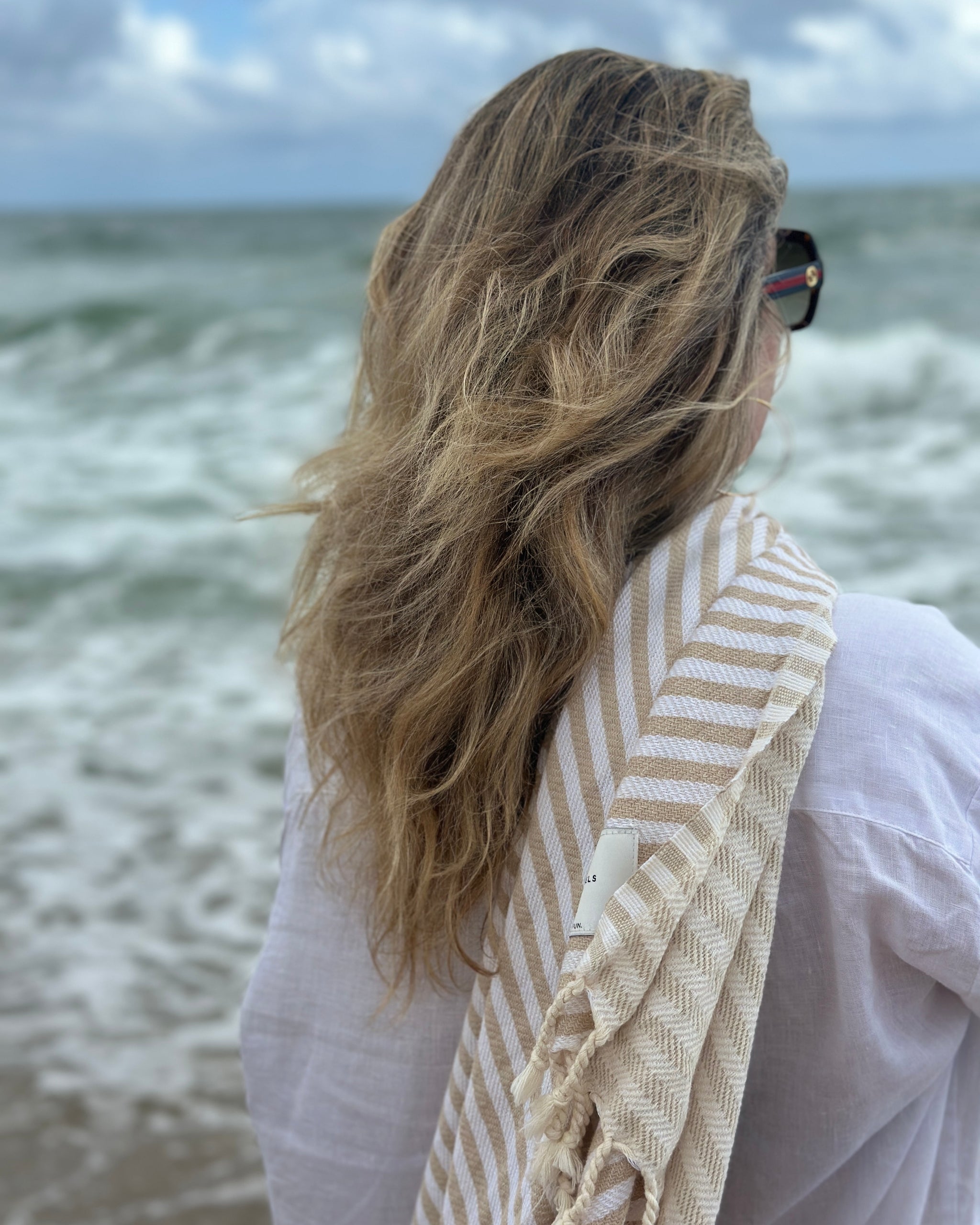 A woman by the sea with a Serena towel over her shoulder