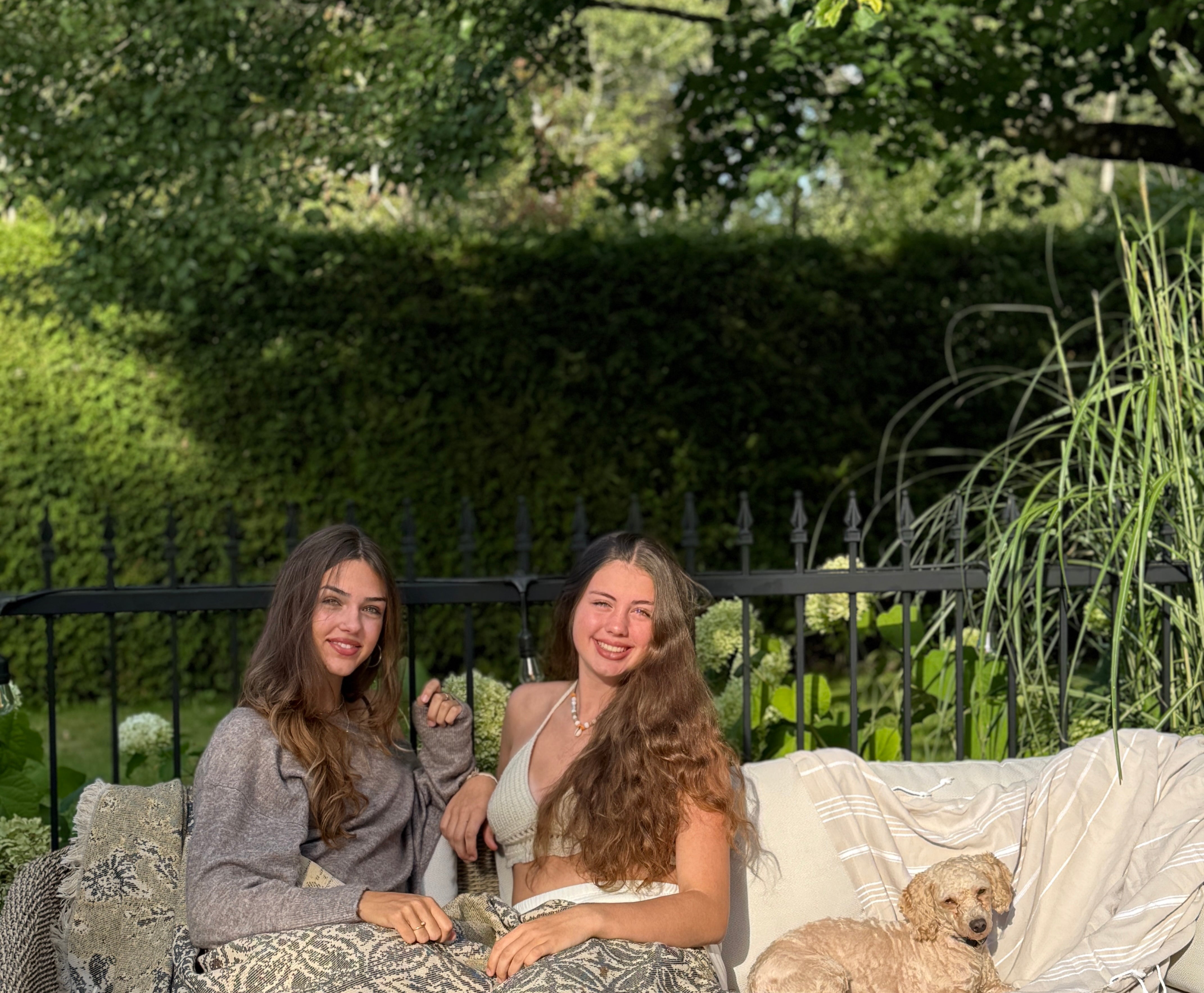 Women smiling wrapped in the Georgie throw made of natural cotton, sitting outdoors in the sun. Soft and chic throw from Balmy’s collection.