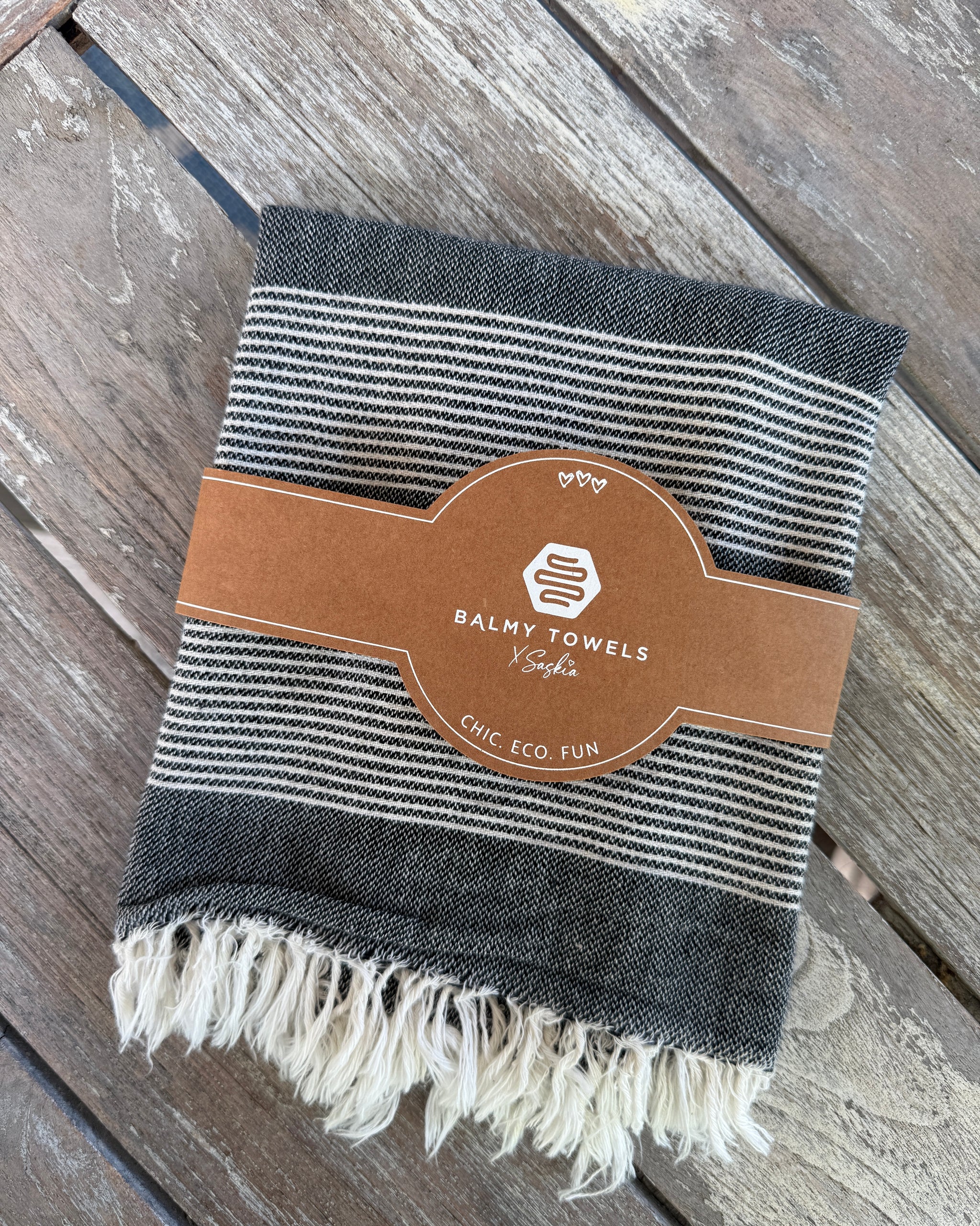 Serviettes à mains CAPE COD charbon pliées sur une terrasse en bois, avec leur bande Balmy CHIC. ECO. FUN.