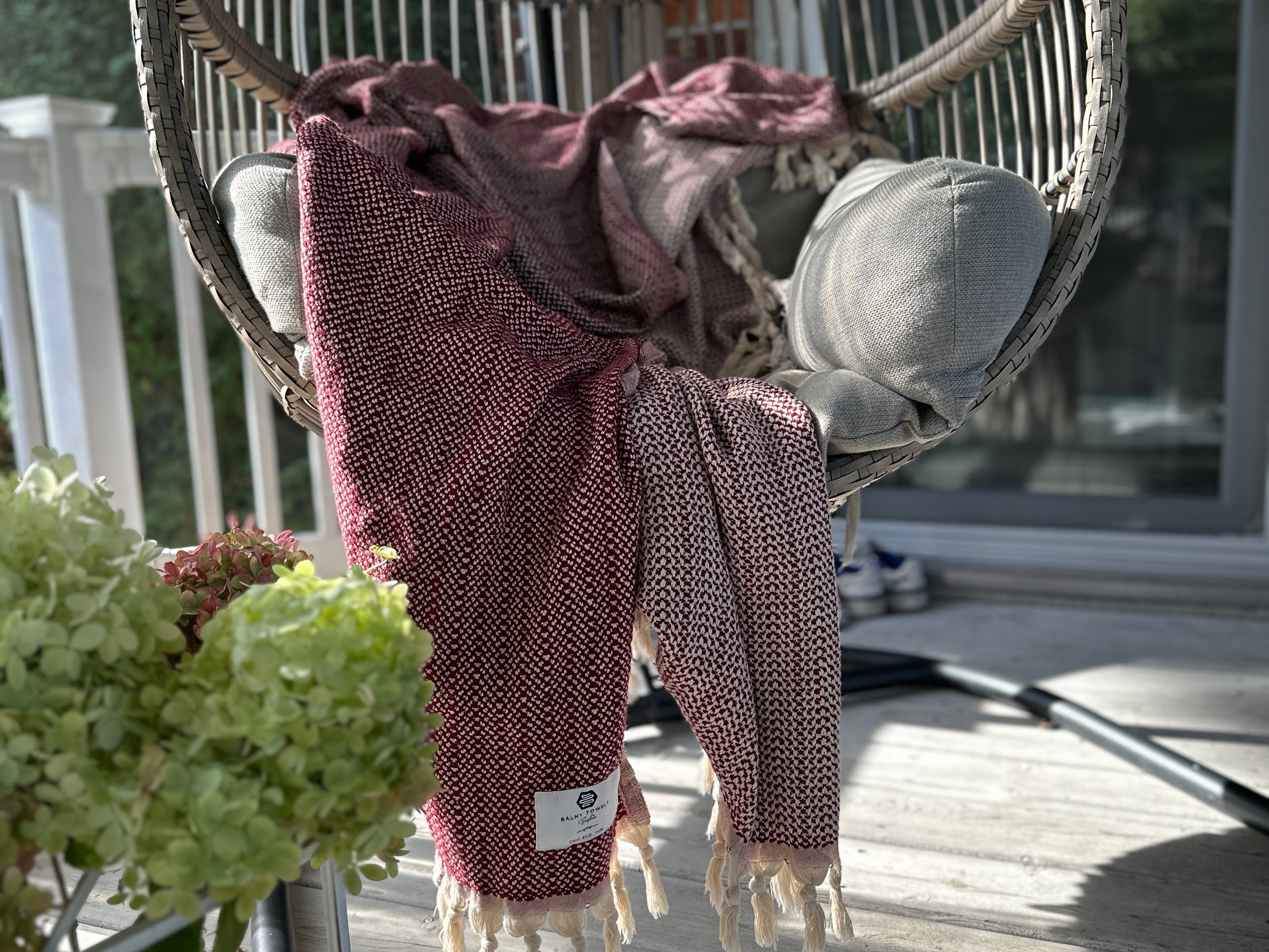 Lionel throw in Burgundy draped over a hanging chair on a sunny patio