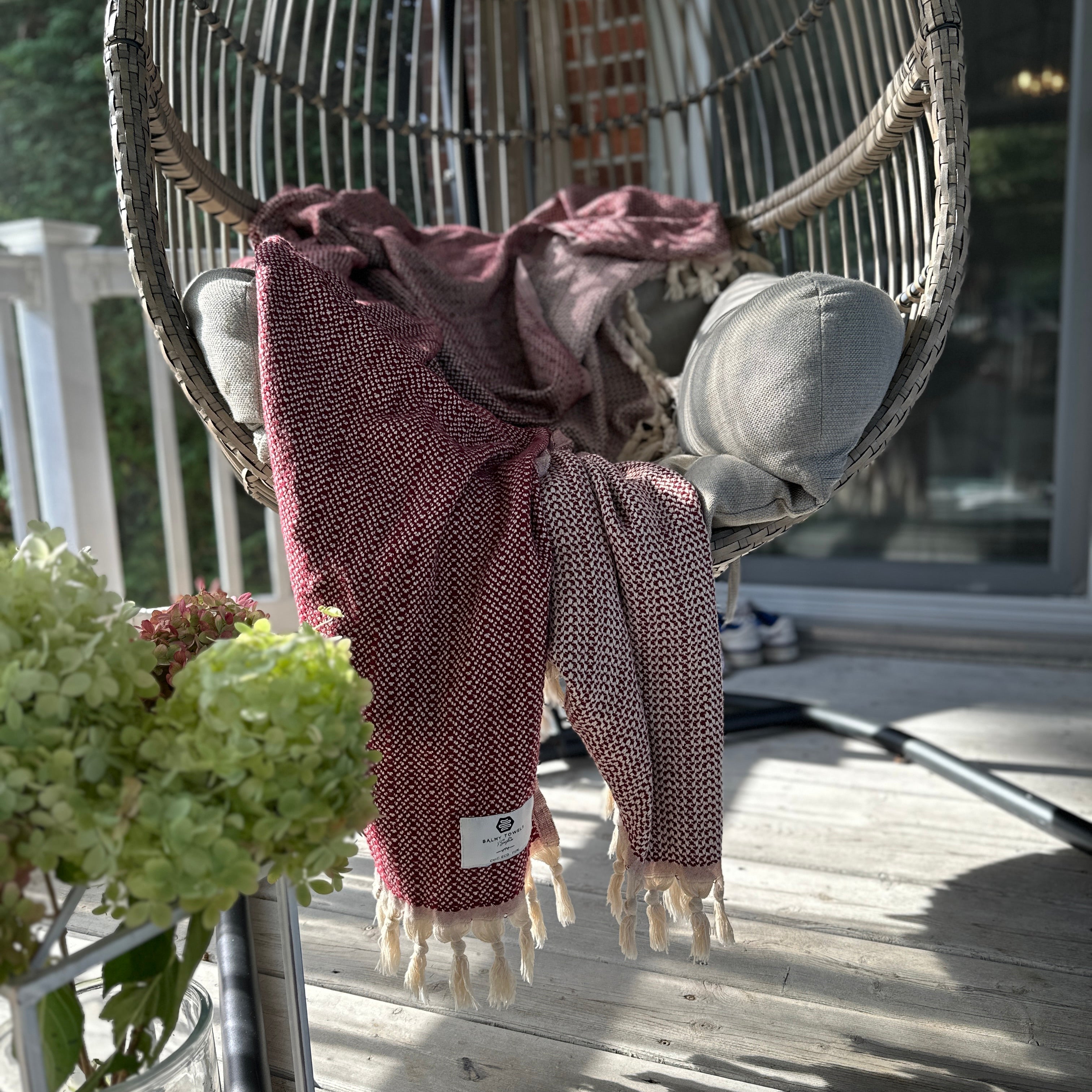 Lionel throw in Burgundy draped over a hanging chair on a sunny patio