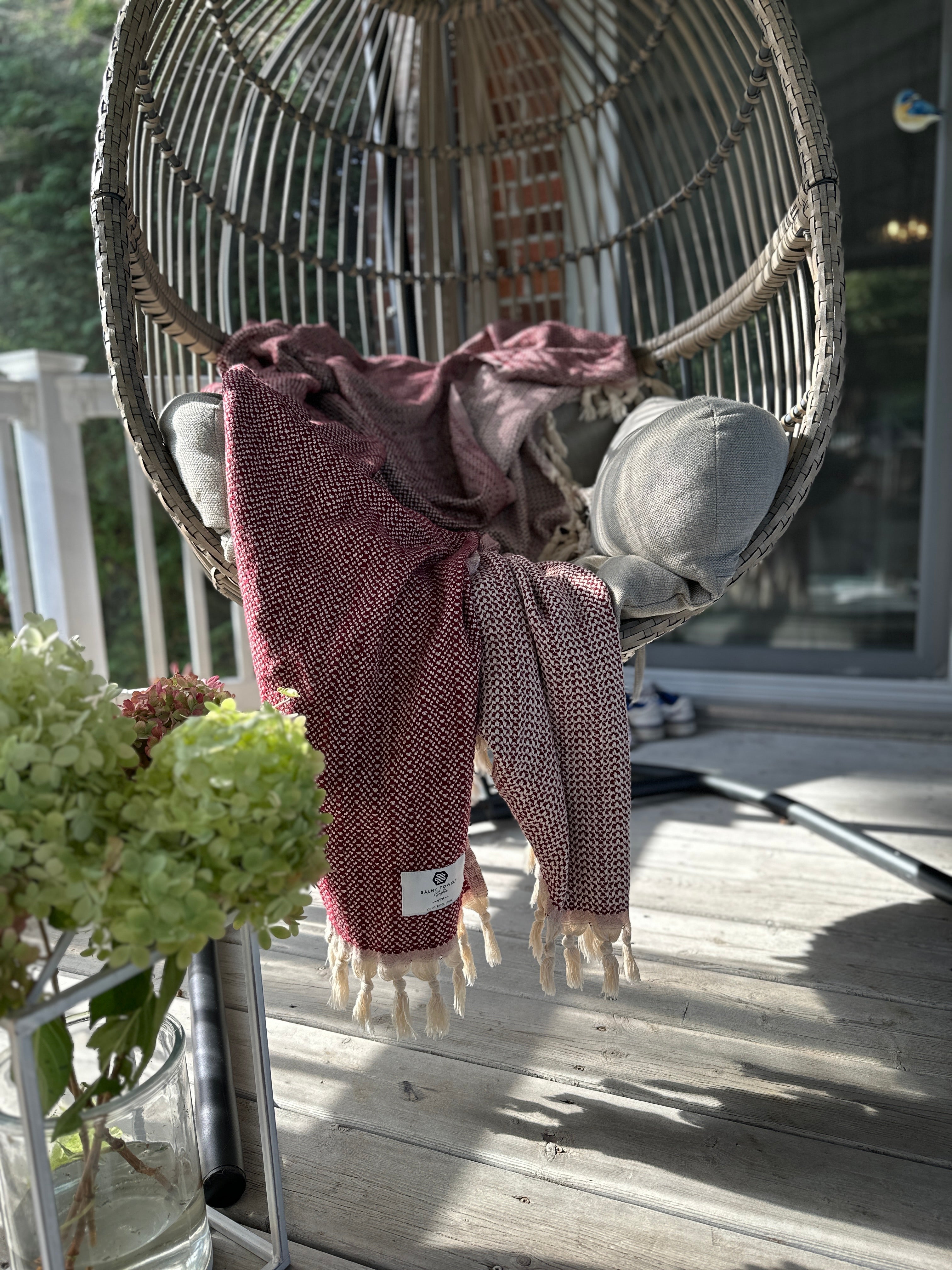 Lionel throw in Burgundy draped over a hanging chair on a sunny patio
