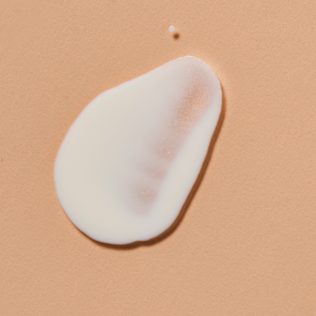 Dollop of white Colorescience No-Show Mineral Sunscreen SPF 50 cream spread on a peach background