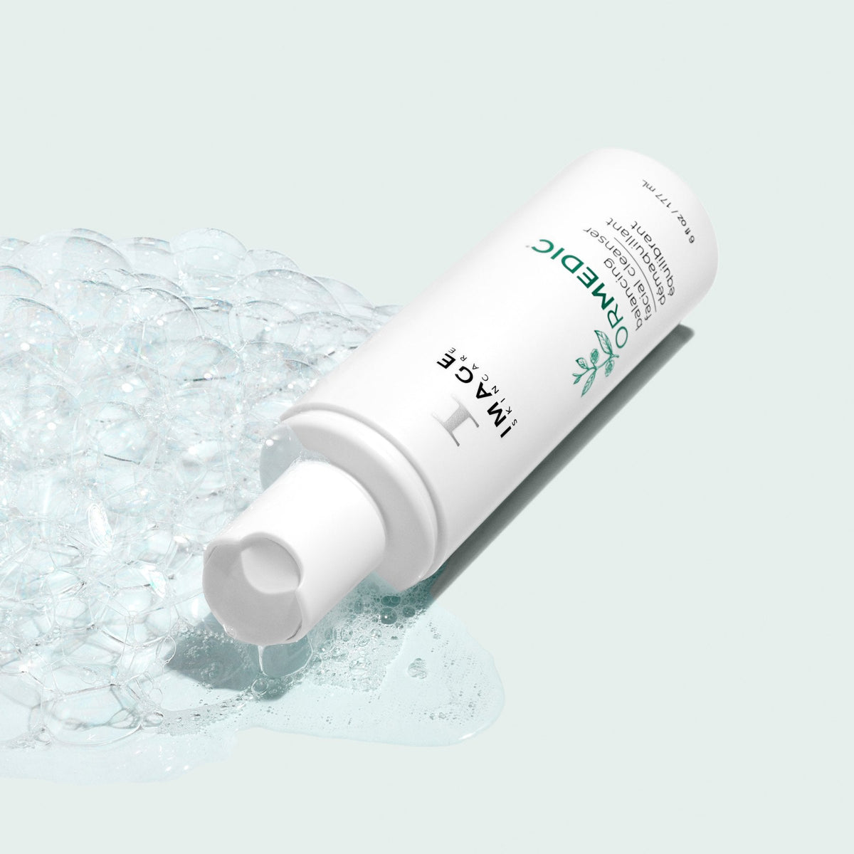 Image Skincare ORMEDIC balancing facial cleanser bottle lying in clear lather, pale green background