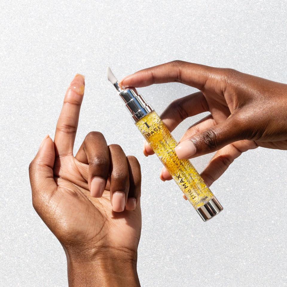 One hand holds the clear Image Skincare the MAX wrinkle smoother tube of golden gel, a drop on the other hand's index finger