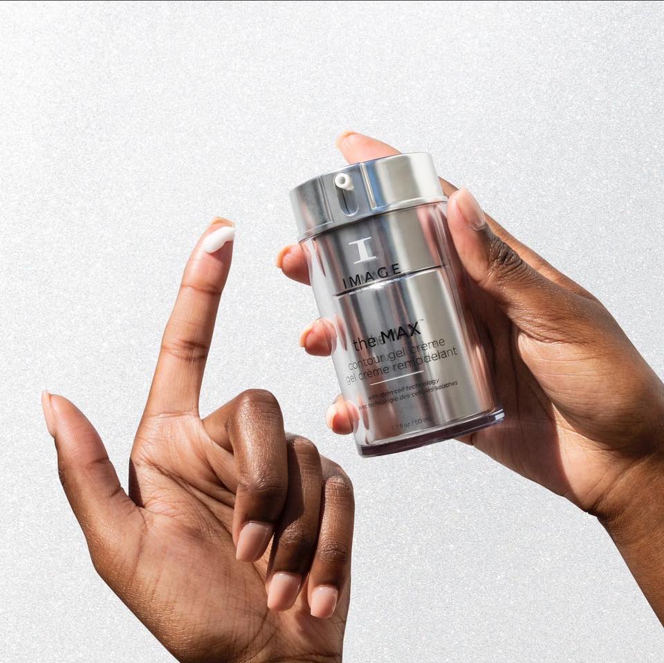 One hand holds the silver Image Skincare the MAX contour gel crème jar, a dab of cream on the other hand's index finger