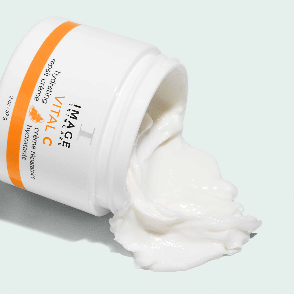 Open white and orange jar on its side, Image Skincare VITAL C hydrating repair crème, white cream spilling out