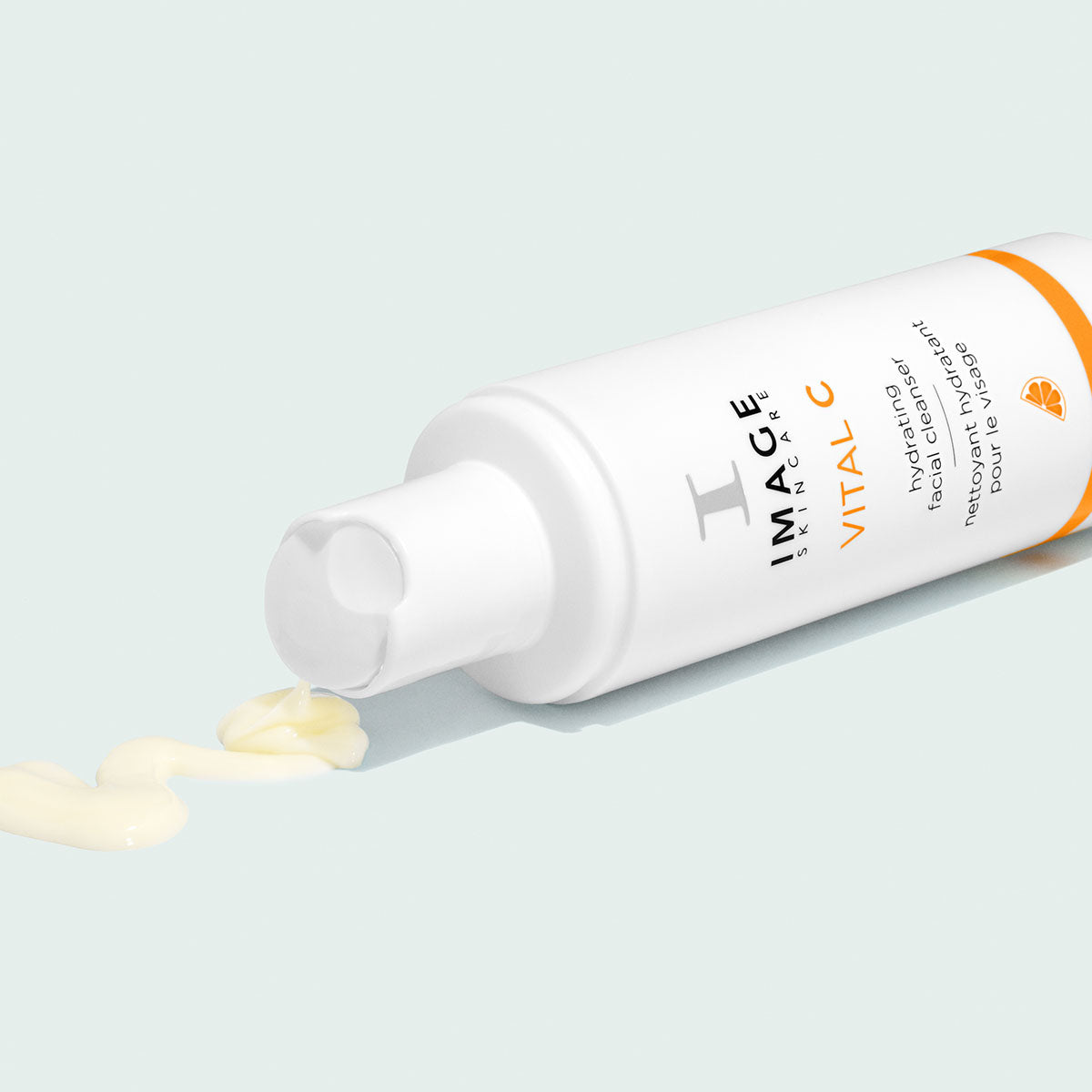 White and orange bottle on its side, Image Skincare VITAL C hydrating facial cleanser, pale yellow cream trail