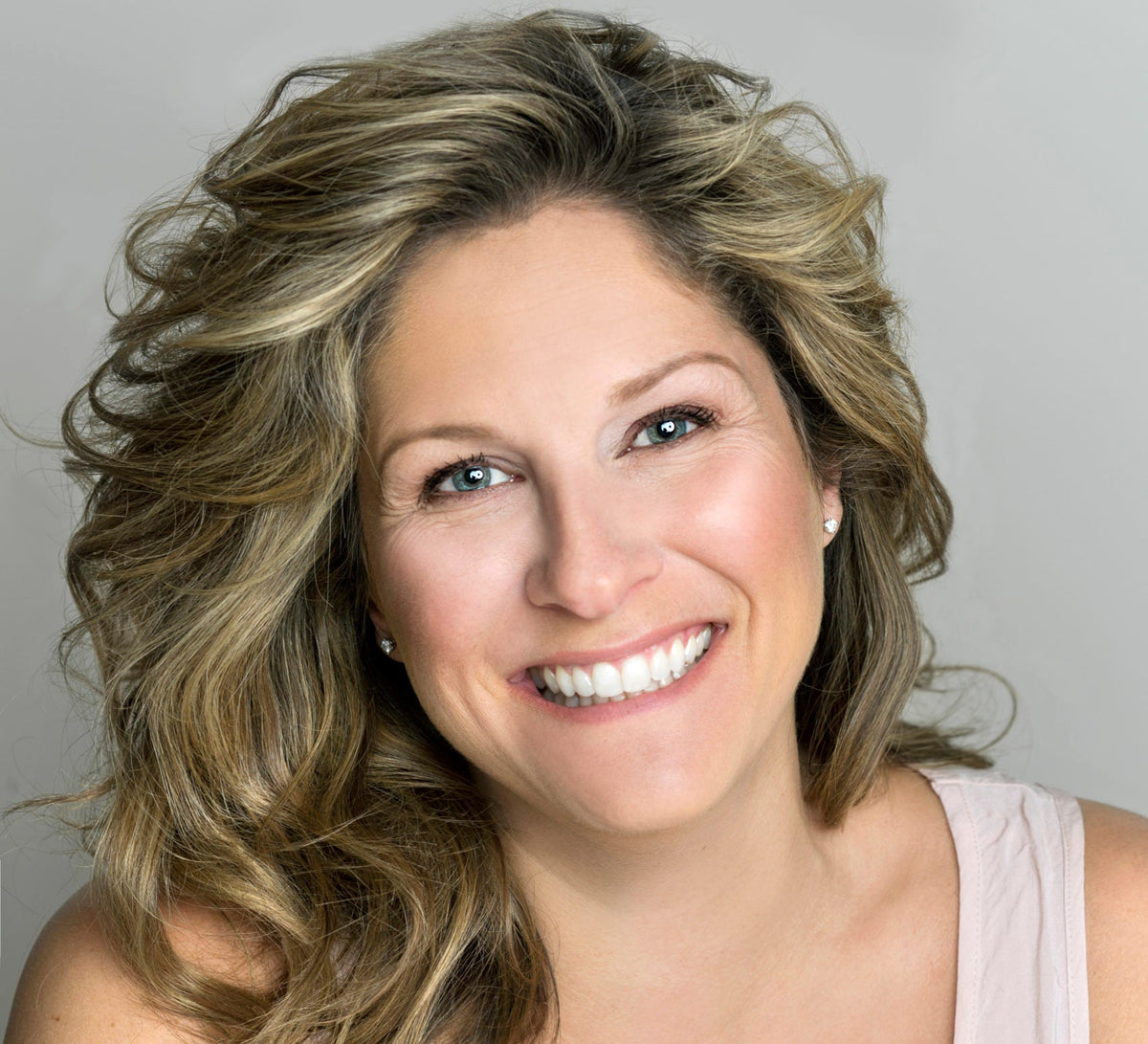 Portrait de Saskia Thuot, souriante, aux longs cheveux blonds ondulés, sur fond gris clair