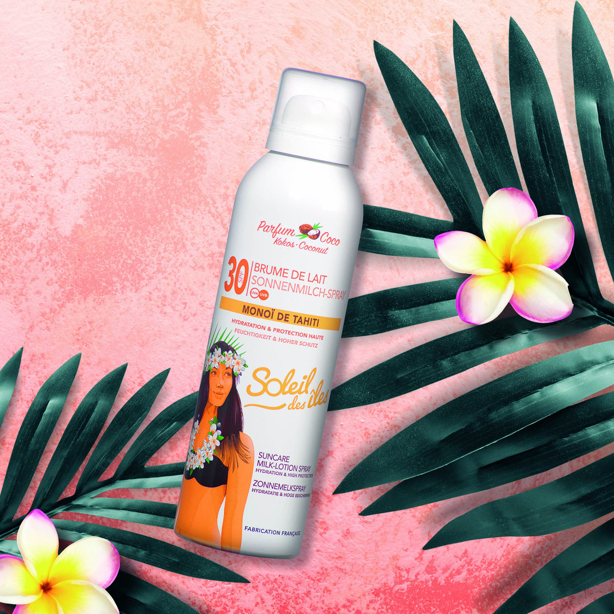 Soleil des Îles SPF 30 coconut milk mist with Monoï de Tahiti can on a pink background with palm leaves and tropical flowers