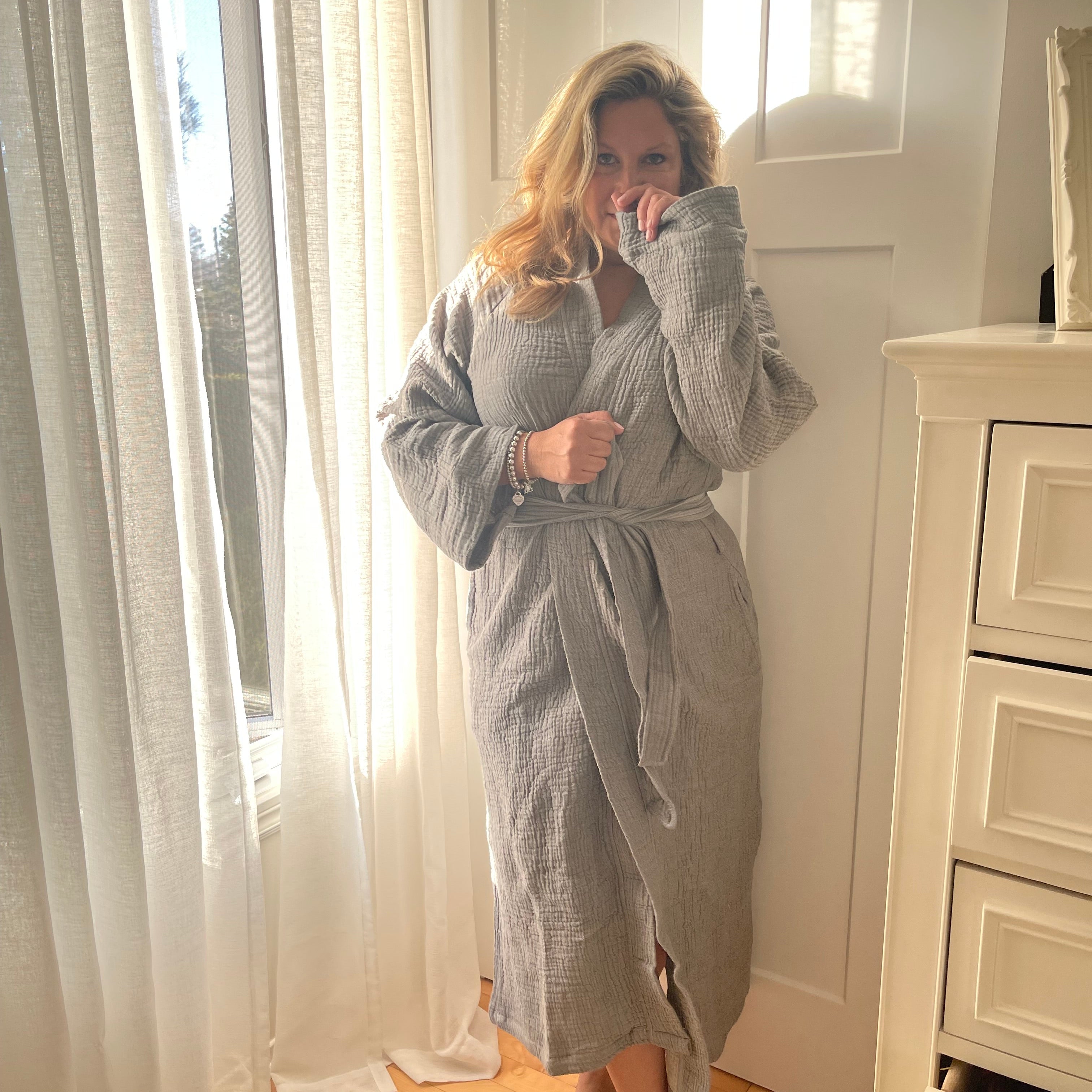 Woman in a bathroom wearing the Bella Bathrobe – Charcoal, handwoven from organic Turkish cotton.
