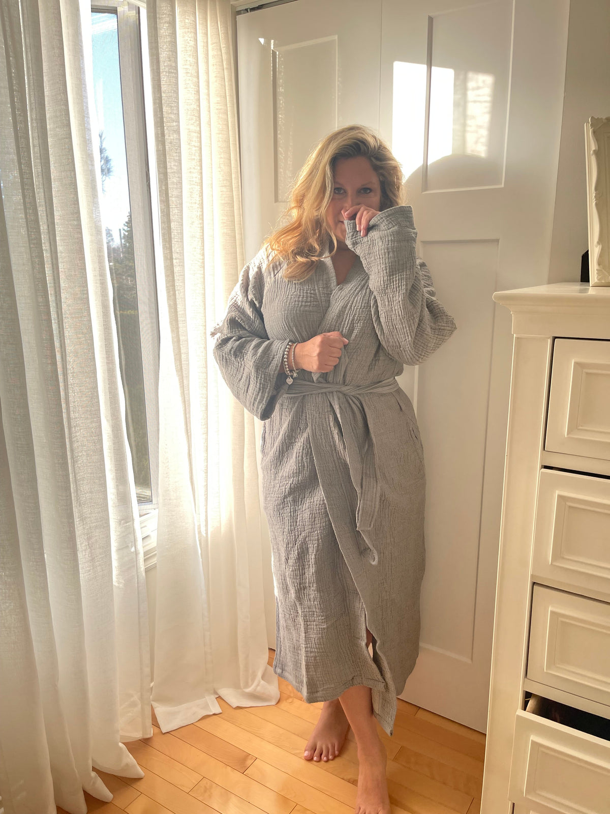 Woman in a bathroom wearing the Bella Bathrobe – Charcoal, handwoven from organic Turkish cotton.
